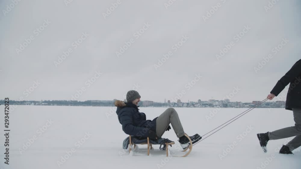 Friends playing on winter nature, pulling a sled with girl, throwing snowballs Friends playing on winter nature, pulling a sled with girl, throwing snowballs
