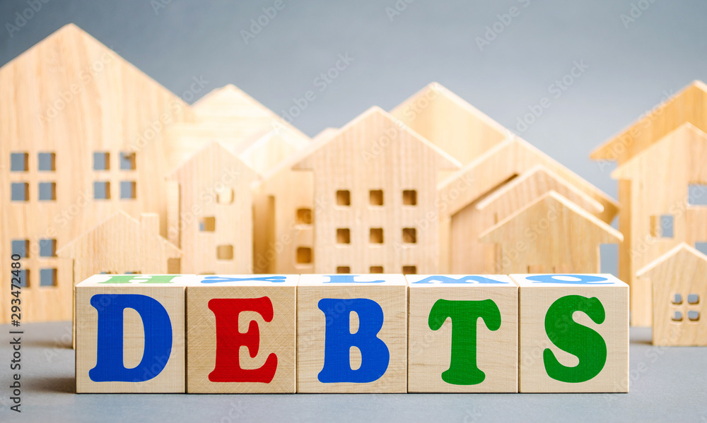 Wooden blocks with the word Debts and miniature houses. Debt concept for housing or mortgage. Real estate and credit, loan Wooden blocks with the word Debts and miniature houses. Debt concept for housing or mortgage. Real estate and credit, loan