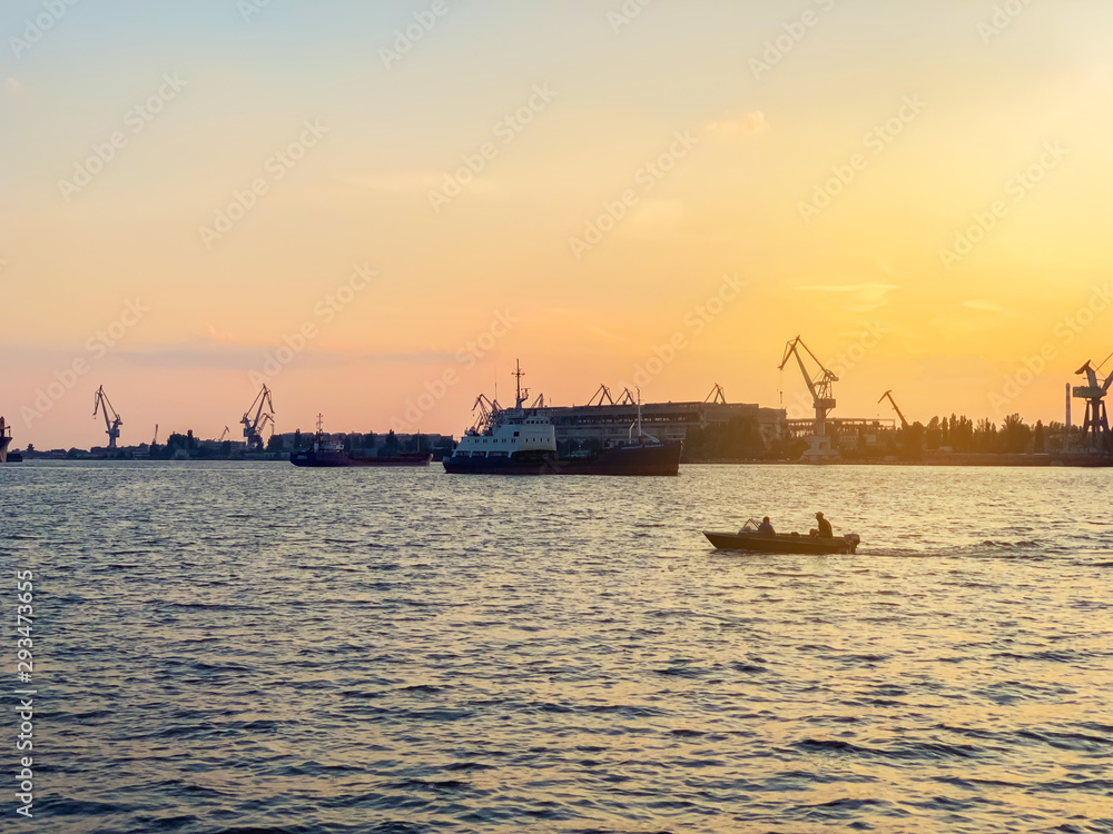 River port with ships at sunset. Busy traffic artery. Logistics and infrastructure. Loading and unloading of ships, trade traffic. Industry and economics. Plants and factories. Transport hub. Dnipro