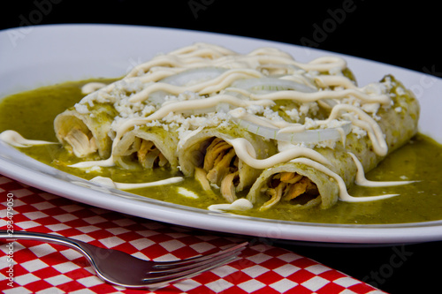 Green enchiladas with jalapeno and tomatillo sauce, fresh crumbled cheese and sour cream, close-up. photo