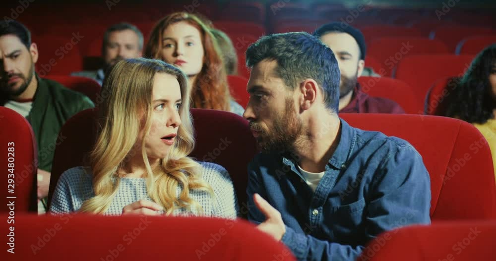 Young Caucasian pretty girl and handsome man sitting together at the date in the cinema and fighting because of the popcorn, then couple behind them asking to be quiet. Young Caucasian pretty girl and handsome man sitting together at the date in the cinema and fighting because of the popcorn, then couple behind them asking to be quiet.