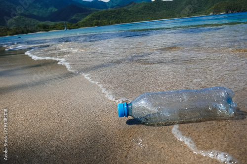 A plastic bottle washed away by the waves on the edge of an empty tropical beach.