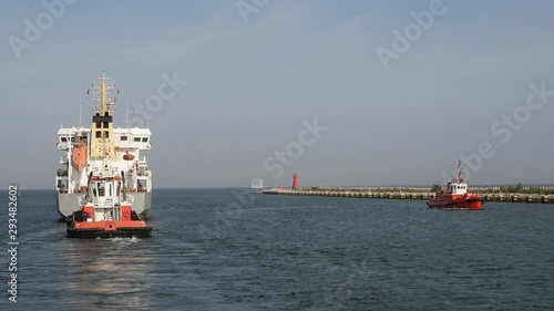 Cargo Ship with Auxiliary Boat goes out from port to the sea at summer day
