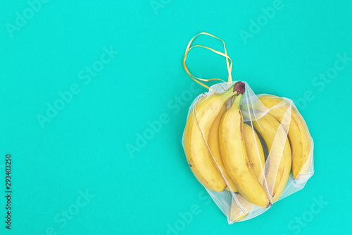 Yellow bananas in reusable eco bags on mint paper background. Fresh fruits in bags from transparent textile for food storage. Plastic free concept. Flat lay. Top View.