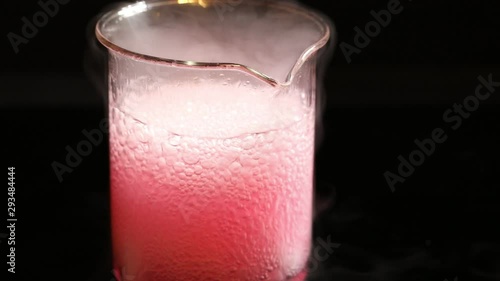 Pink chemical substance that boils in a becker isolated on a black background