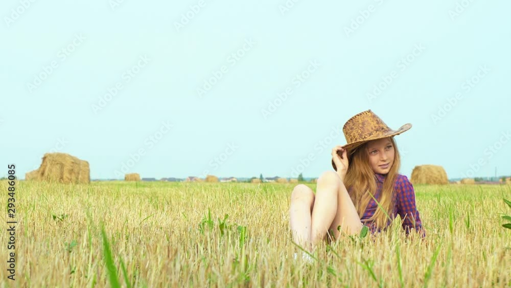 Cute girl in cowboy hat posing at photo session on rural field with haystack. Teenager girl in cowgirl look posing for camera on haystack background at harvesting field Cute girl in cowboy hat posing at photo session on rural field with haystack. Teenager girl in cowgirl look posing for camera on haystack background at harvesting field