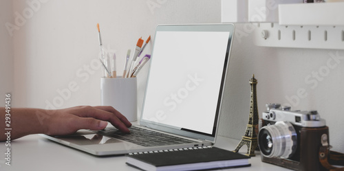 Young man typing on blank screen laptop computer in minimal artist workspace