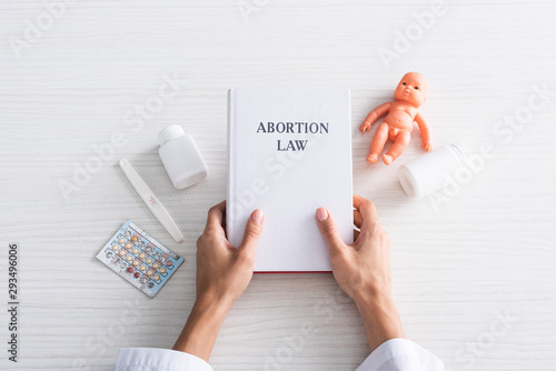 Foto top view of woman holding book with abortion lettering near baby doll and aborti