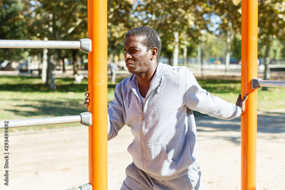 Fototapeta premium Young male training different exercises at chin-up bar in park outdoor