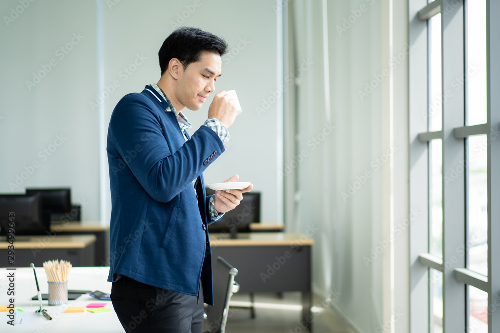 Portrait of smart and handsome young businessman drinking a coffee and looking outside of the window close up.