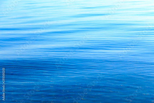Fototapeta Naklejka Na Ścianę i Meble -  Clear water texture in blue and orange. Background of the ocean and the sea backlit by the sun. Soft waves. Natural water