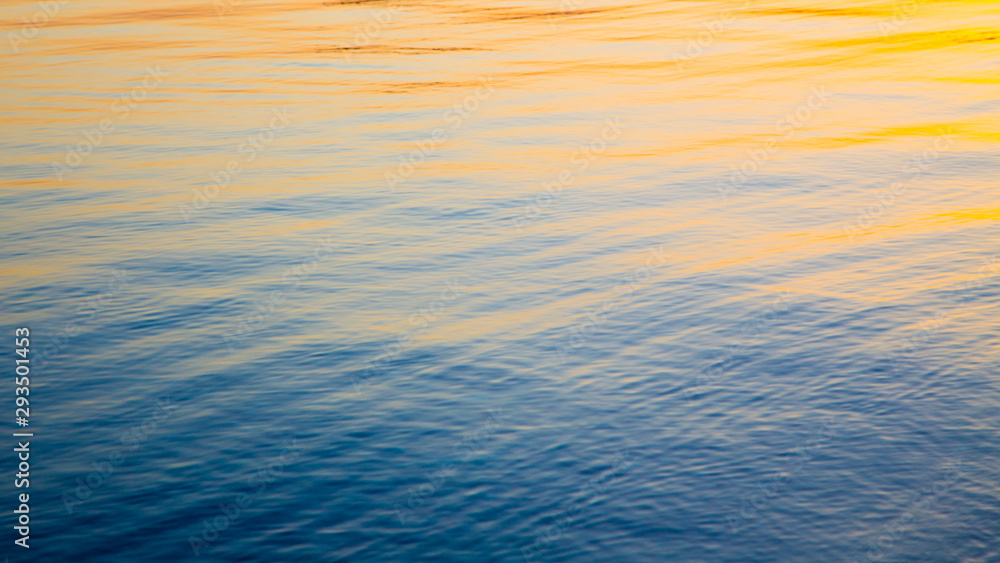 Clear water texture in blue and orange. Background of the ocean and the sea backlit by the sun. Soft waves. Natural water - obrazy, fototapety, plakaty 