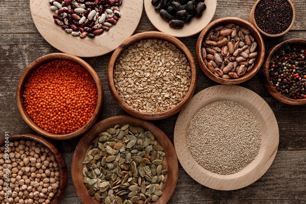 top view of bowls with raw oatmeal, red lentil, various beans, quinoa, chickpea, peppercorns and pumpkin seeds on wooden surface top view of bowls with raw oatmeal, red lentil, various beans, quinoa, chickpea, peppercorns and pumpkin seeds on wooden surface