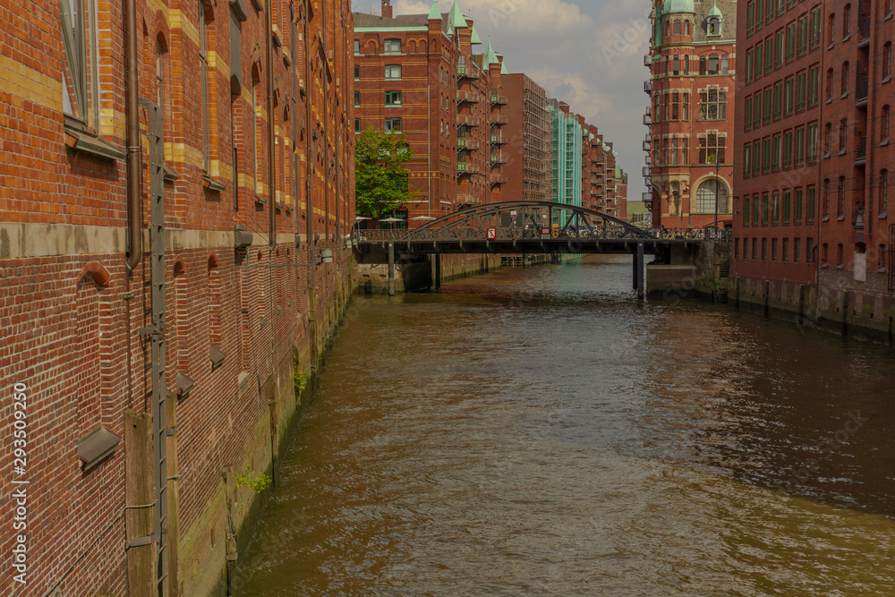 a river through hamburg with big red houses and in the background a bridge