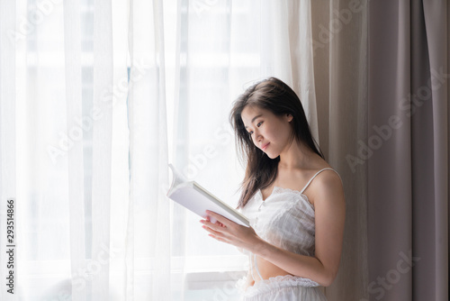 Asian women while reading book near window with shear curtain / bedroom concept / copy space