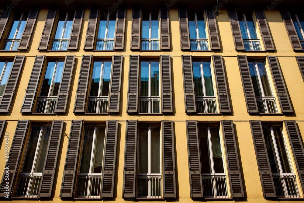 Close up. Symmetrical windows with wooden shutters in an Italian traditional building in the center of Milan, Lombardy, Italy. European modern architecture. Street view of the building facade.