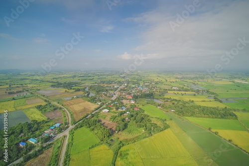 Aerial view morning above green rice paddy fields and village in rainy season around with soft fog with cloudy sky background, Lam Phayom village in Ban Pong, Ratchaburi, west Thailand.