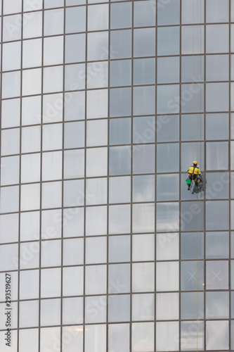 A man worker in worksuit cleaning the exterior windows of a skyscraper - industrial alpinism - hanging on ropes photo