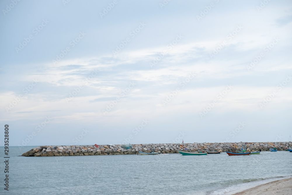 Close up the temporary pear or port in small harbour with stone docks in area of Thai shore,small Thai fishing boats parking around on blue sky background in the sea,Thailand