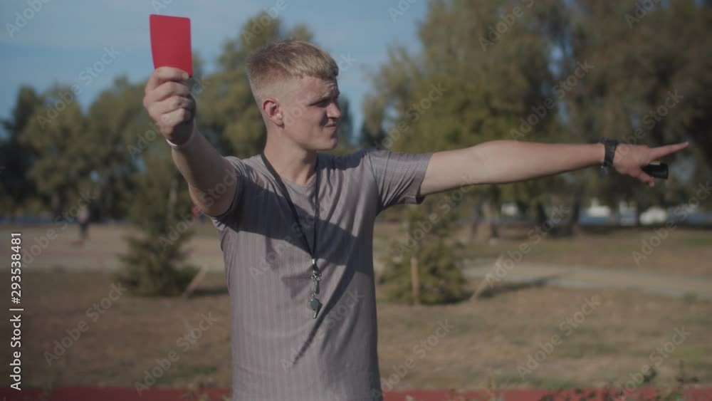 Determined football referee whistling and indicating red card dismissal