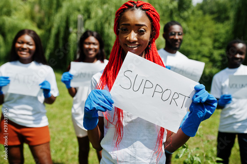 Group of happy african volunteers hold blank board with support sign in park. Africa volunteering, charity, people and ecology concept.
