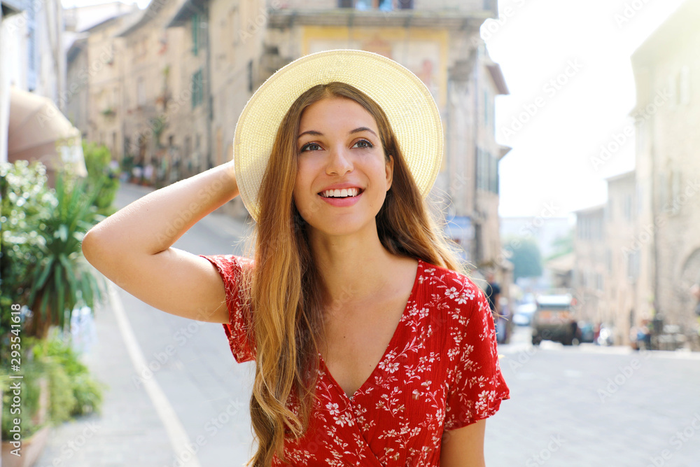 Sunny lifestyle fashion portrait of young  woman walking on the street with red dress and hat. Traveling in Italy.