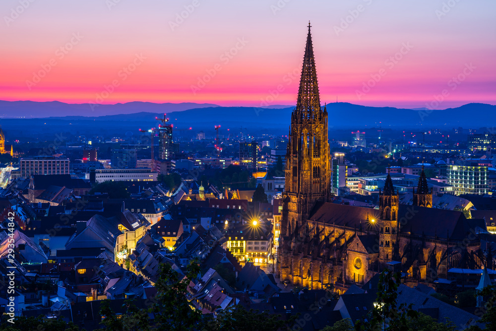 Germany, Intense red afterglow sky decorating beautiful skyline of black forest city freiburg im breisgau and famous illuminated church muenster by night