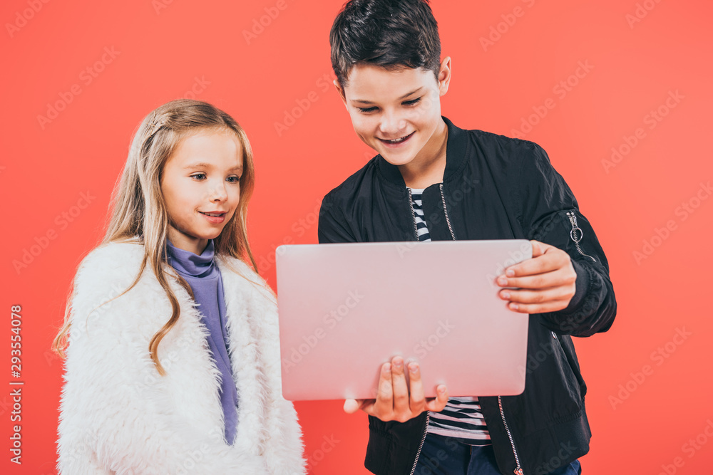 two smiling kids using laptop isolated on red two smiling kids using laptop isolated on red