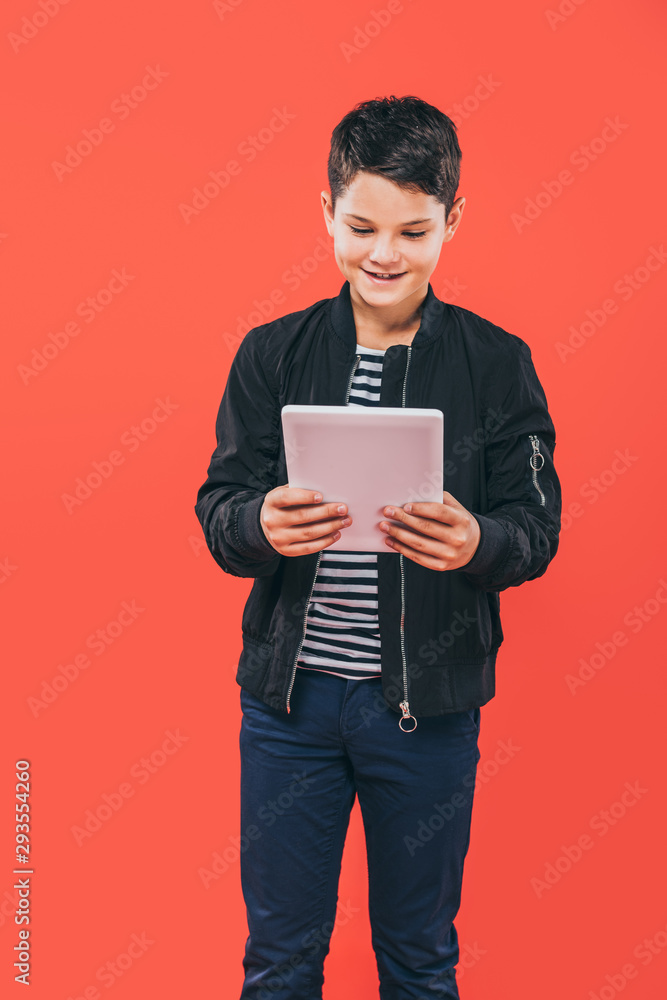 smiling kid in jacket using digital tablet isolated on red smiling kid in jacket using digital tablet isolated on red