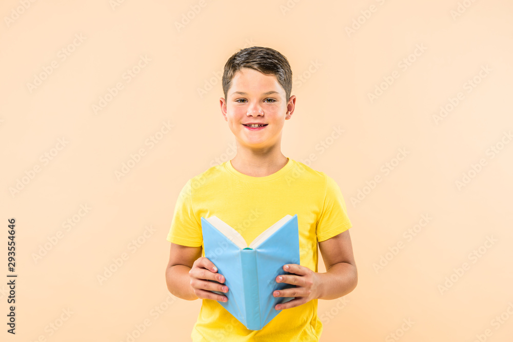 front view of boy in yellow t-shirt holding book isolated on pink front view of boy in yellow t-shirt holding book isolated on pink