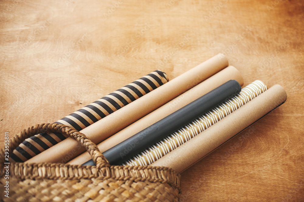 Stylish christmas wrapping paper rolls in rustic straw basket on wooden table, copy space. Preparation for winter holidays. Craft, black and gold wrapping papers Stylish christmas wrapping paper rolls in rustic straw basket on wooden table, copy space. Preparation for winter holidays. Craft, black and gold wrapping papers