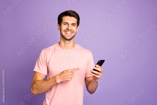 Portrait of his he nice attractive cheerful cheery glad content guy wearing pink tshirt holding in hands recommending digital device isolated on violet purple lilac pastel color background © deagreez
