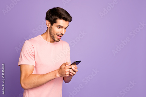 Profile side view portrait of his he nice attractive cheerful glad focused guy wearing pink tshirt holding in hands using digital device gadget isolated on violet purple lilac pastel color background © deagreez