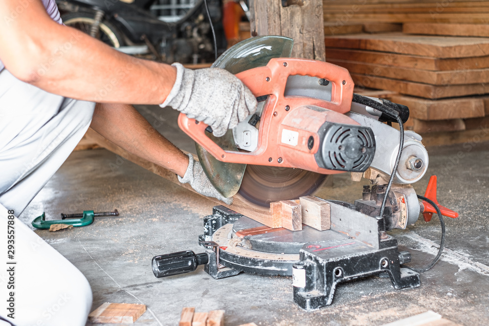 Close up of carpenter hand wearing safety glove cutting a timber woods with compound miter or angle saw in workshop place.