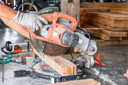 Close up of carpenter hand wearing safety glove cutting a timber woods with compound miter or angle saw in workshop place.