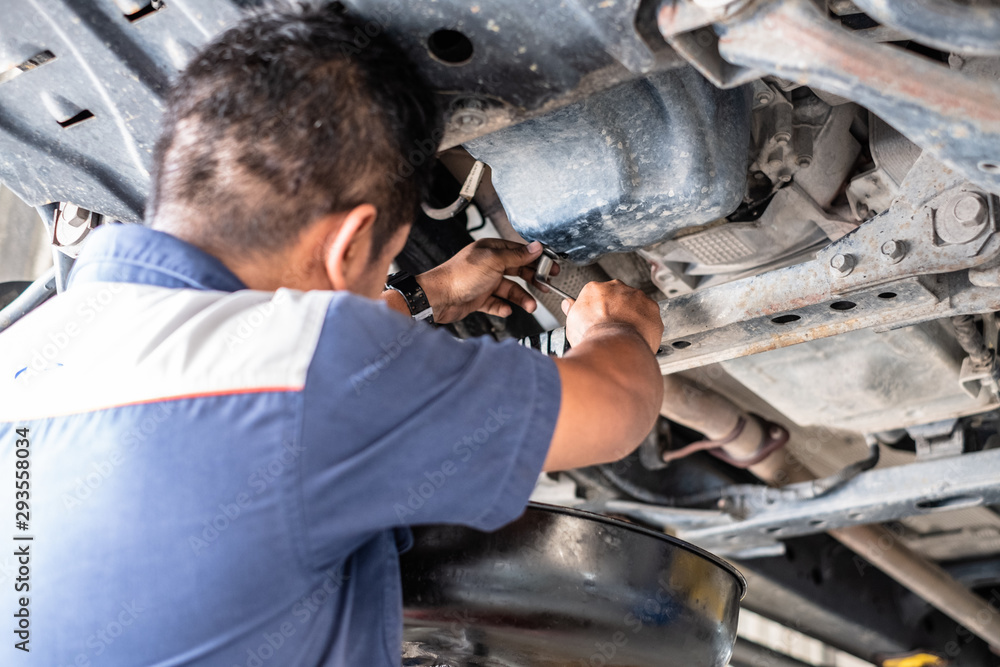Thai mechanic fix car at the garage and change engine oil. He standing under the car on lift machine. Thai mechanic fix car at the garage and change engine oil. He standing under the car on lift machine.