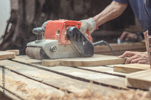 Carpenter sanding wood with belt sander at workshop in wooden cutting board project or woodworking carpentry