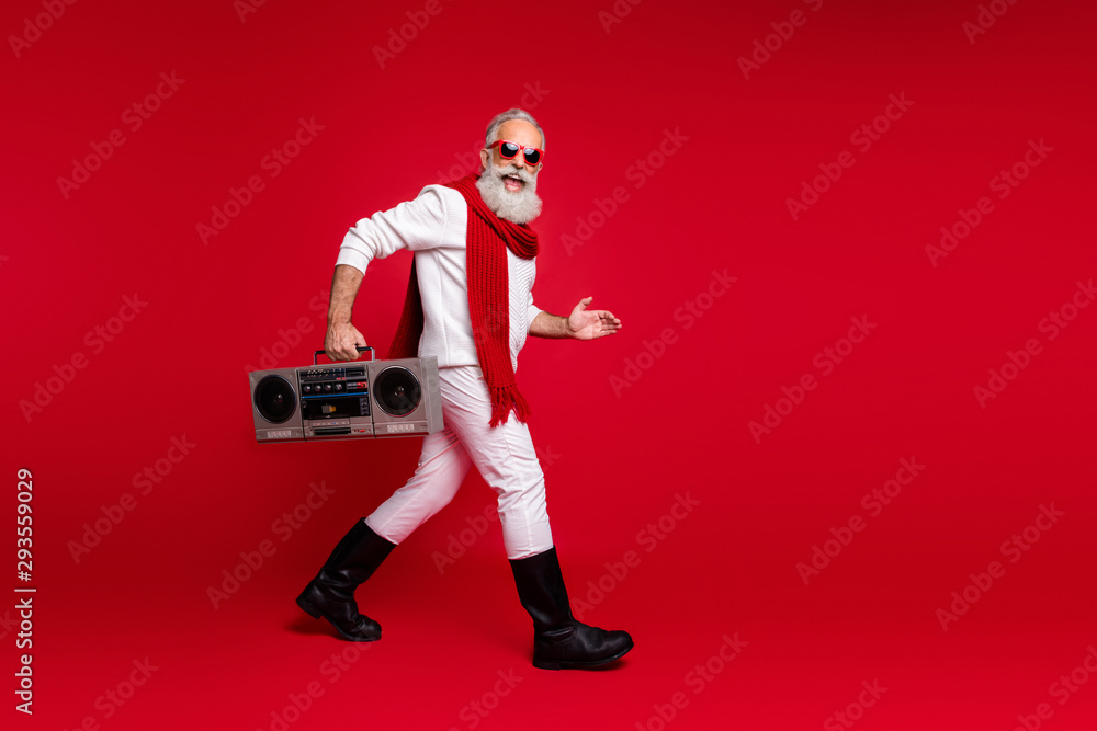 Full body profile side photo of excited grandfather going holding audio cassette wearing white sweater isolated over red background Full body profile side photo of excited grandfather going holding audio cassette wearing white sweater isolated over red background