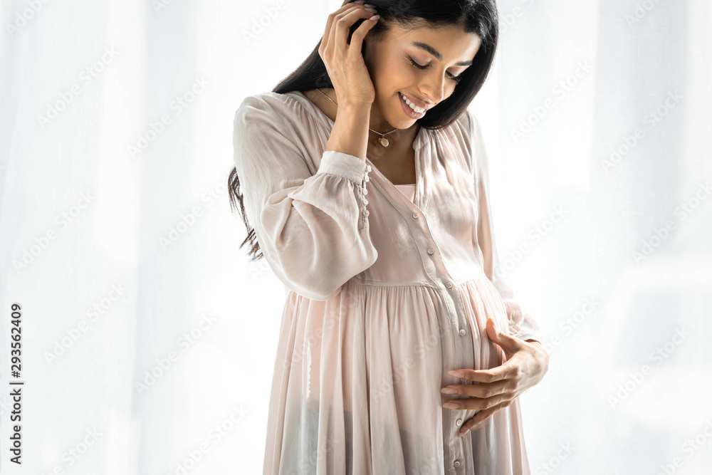 smiling pregnant african american woman hugging belly in apartment smiling pregnant african american woman hugging belly in apartment