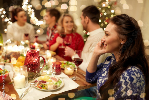 holidays, communication and celebration concept - happy young woman calling on smartphone and having christmas dinner with friends at home