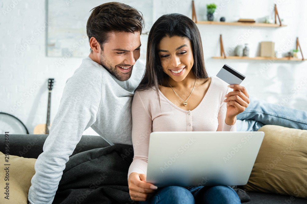 african american woman holding credit card and looking at laptop with man african american woman holding credit card and looking at laptop with man