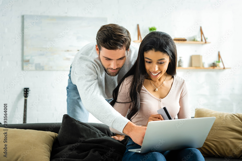 african american woman holding credit card and looking at laptop with man