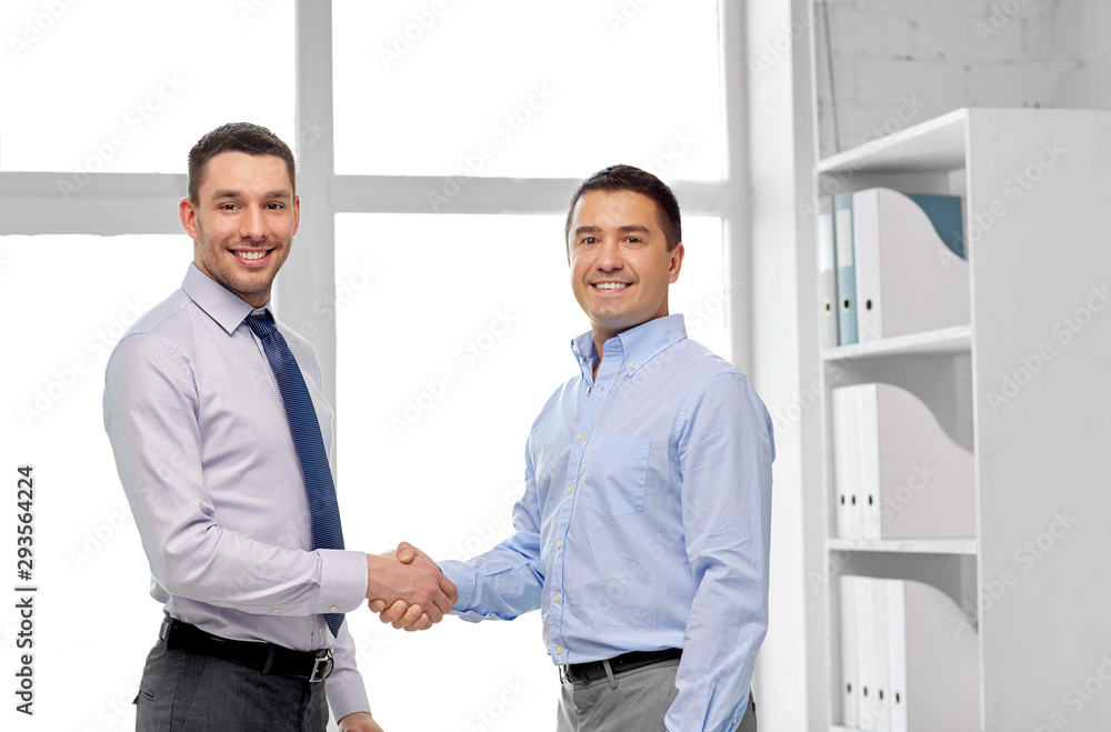 business, gesture and partnership concept - happy businessmen making handshake at office
