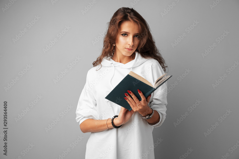 Student girl teenager in white hoodie holding a book in her hands over a grey background Student girl teenager in white hoodie holding a book in her hands over a grey background