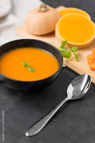 food, new nordic cuisine, culinary and cooking concept - close up of vegetable pumpkin cream soup in bowl and spoon on stone table