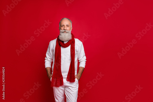 Trendy senior man santa like style holding hands in pockets wear warm knitted clothes isolated red background © deagreez