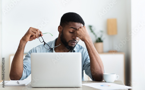 Tired african american employee having headache after working on laptop photo