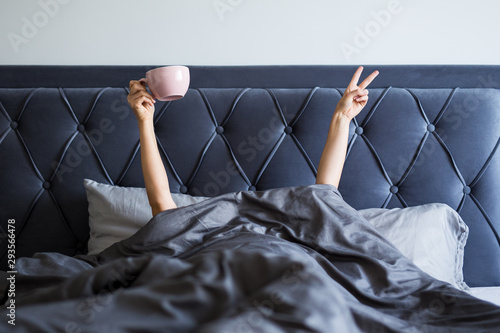 good morning concept - female hands with coffee mug and victory sign sticking out from the blanket photo