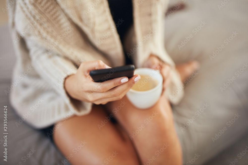 Top view of caucasian woman using smart phone and holding cup of coffee while sitting on bed in morning. Top view of caucasian woman using smart phone and holding cup of coffee while sitting on bed in morning.