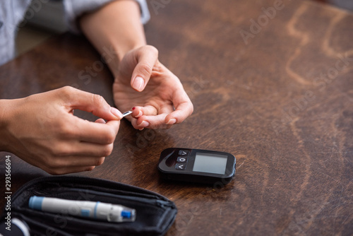 cropped view of woman doing blood test near glucose monitor